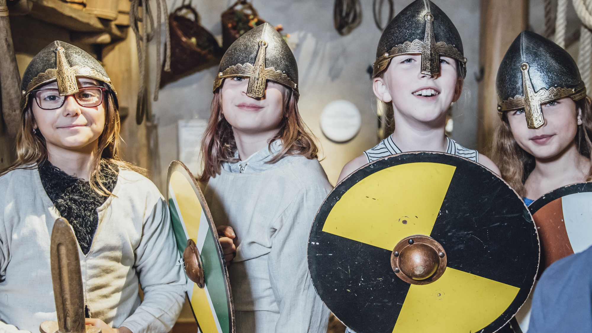 Four children wearing helmets and shields. They are smiling.