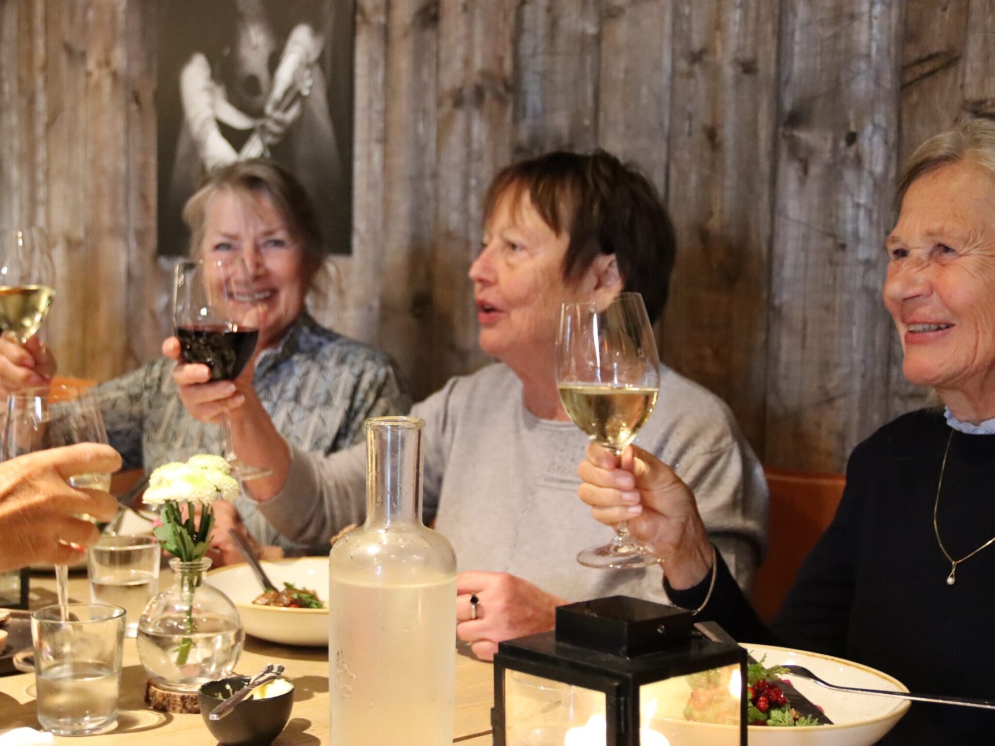 Three women sitting at a restaurant table, holding up wine glasses and smiling.