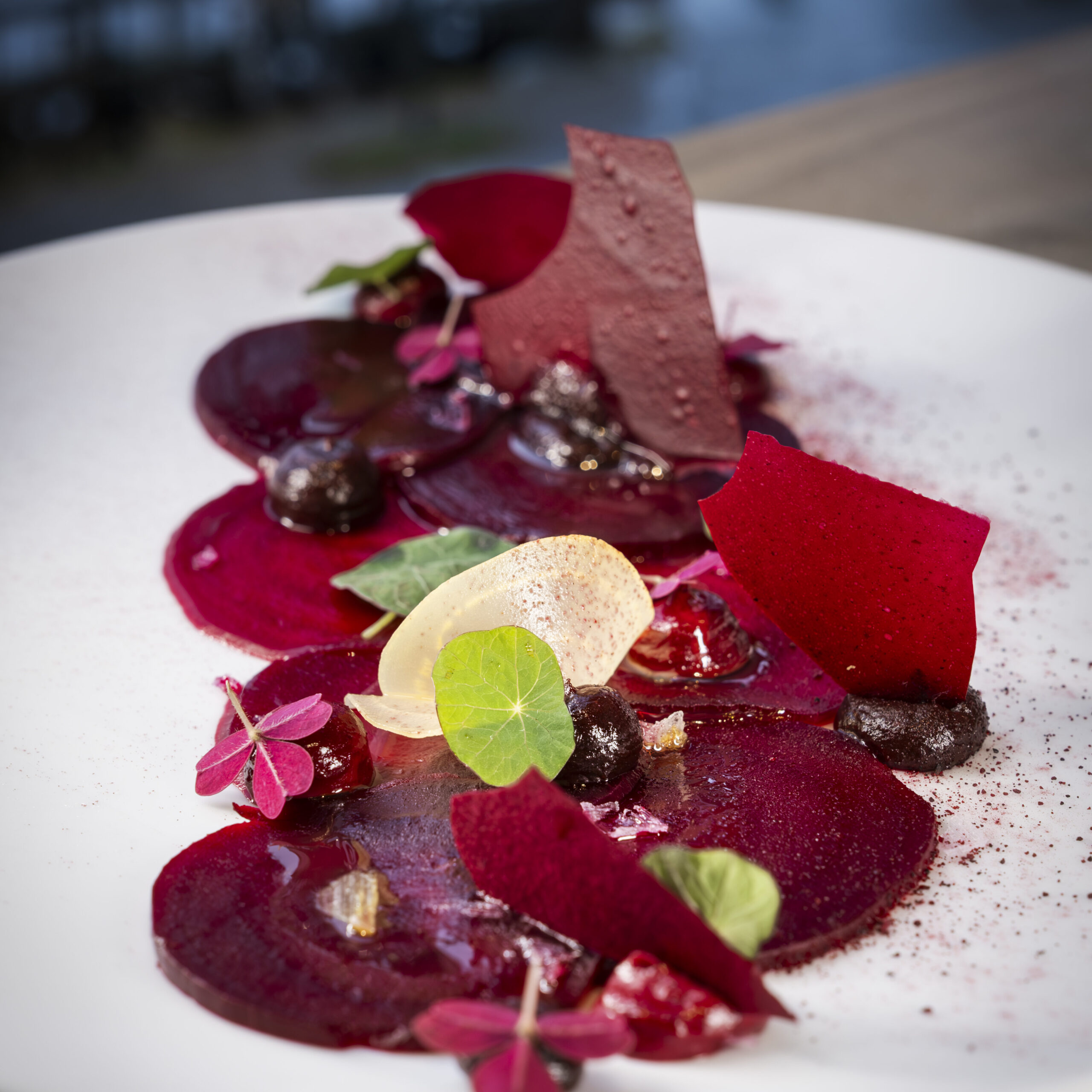 A dish featuring red and pink hues, garnished with flowers and leafy greens.