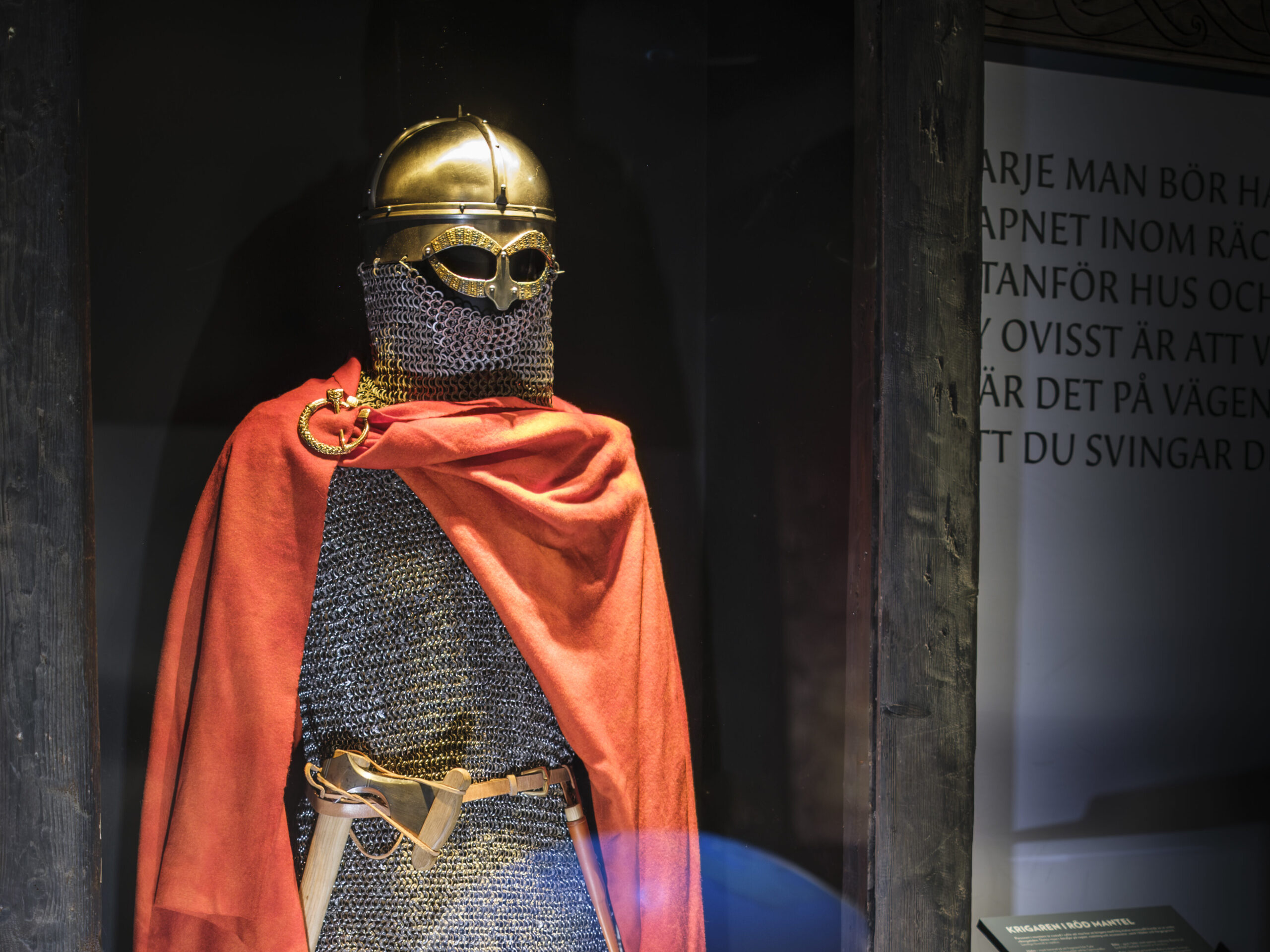 A Viking dressed in Viking Age clothing stands inside a glass display case.